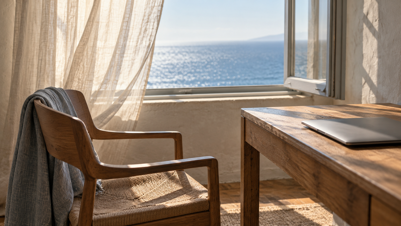 Empty chair and closed laptop beside an open coastal window, suggesting a deliberate pause from work