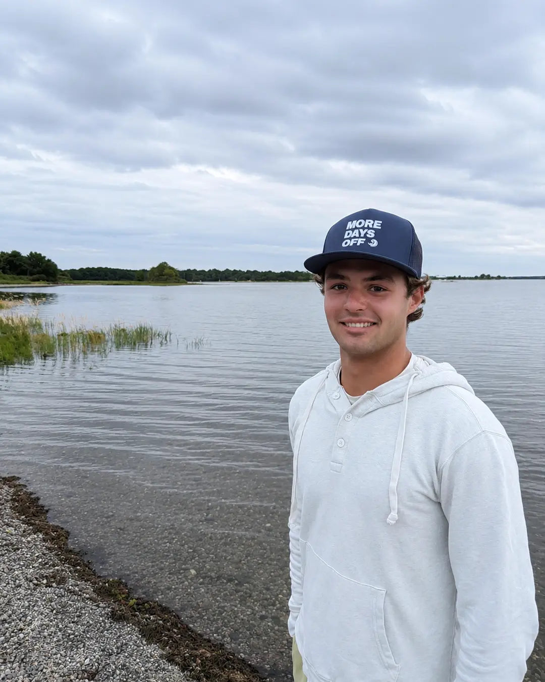 Model wearing the navy More Days Off hat on the shoreline