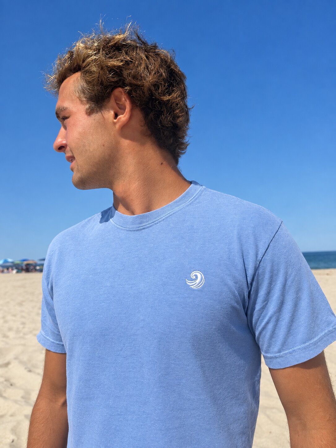 Close-up of the white Healing Wave embroidery on the denim blue tee