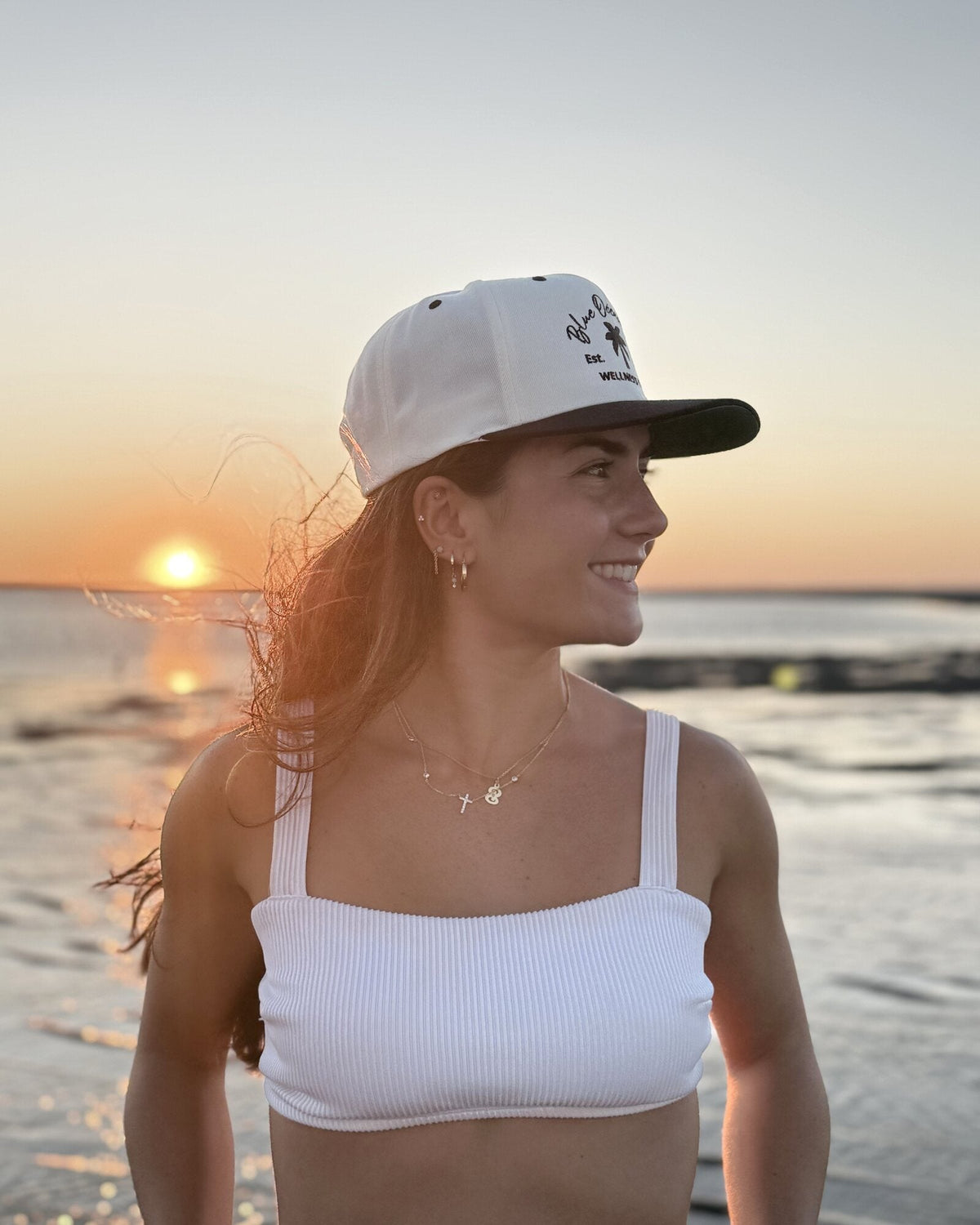 Woman wearing the Blue Ocean Life Wellness Club Snapback Hat in a right-side profile at sunset